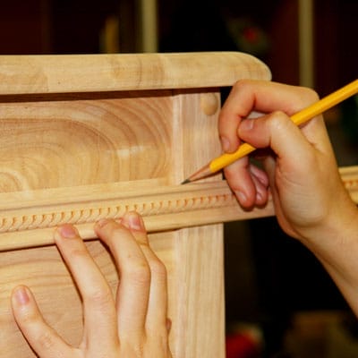 A person using a pencil to mark and measure the apron of a table trim.