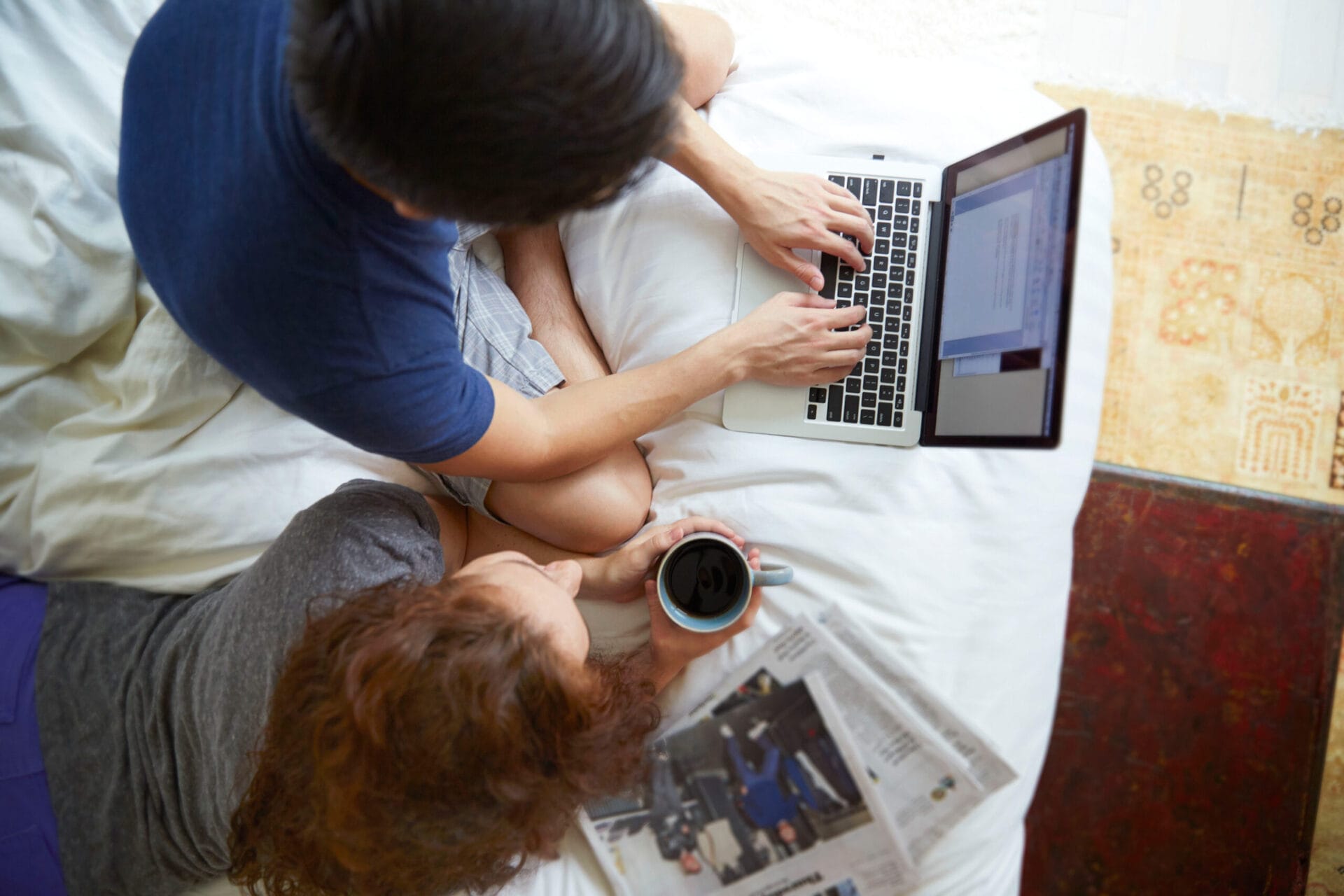 A couple sitting on a bed in front of a laptop, planning a kitchen redesign