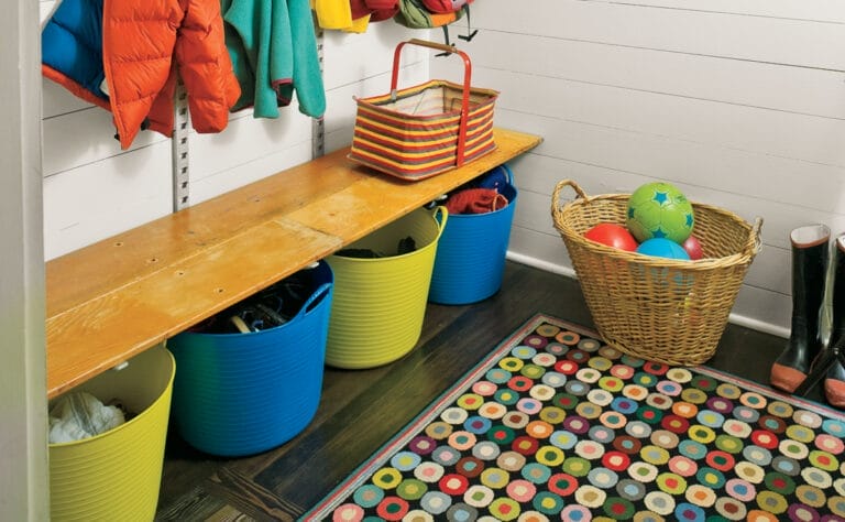 an up close view of colorful baskets on the floor of a mudroom that hold balls and toys