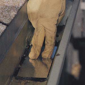 Person with gloved hands pressing down on a metal patch to repair a damaged gutter.