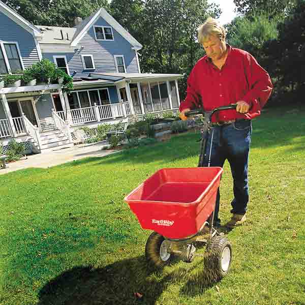 A man pushing a wheelbarrow over a lawn in front of a house.