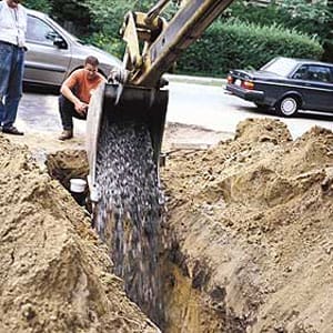 A backhoe dropping crushed stone into a trench.