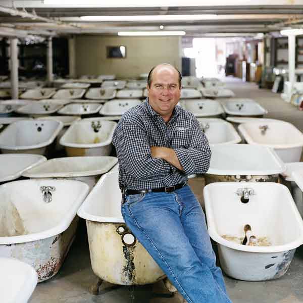 Richard sitting on an old bathtub in a room full of bathtubs.