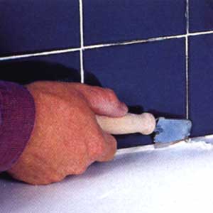 Image of a person removing the old caulk on ceramic tiles