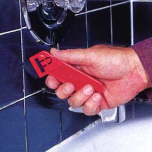 Image of a person using a grout saw to scratch out old grout between ceramic tiles