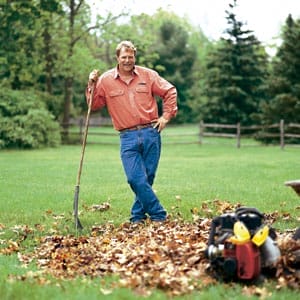 Man standing with a rake next to a pile of leaves.