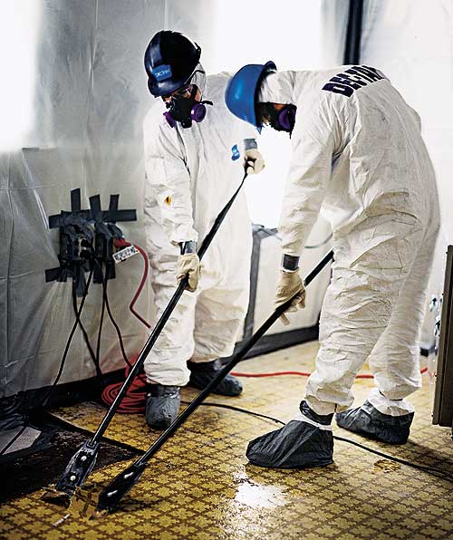 Two men in an asbestos abatement crew removing asbestos from the floor of a home.