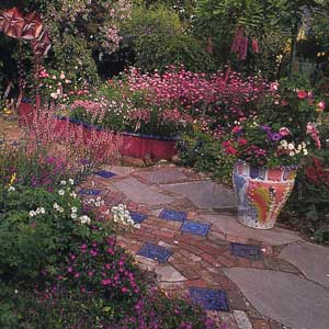 A path made of bricks, ceramic tiles, and stones going through a flowering garden.
