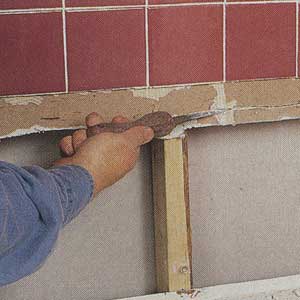 A man shows how to trim the broken edge of the existing gypsum wallboard with a drywall saw to create a neat, straight horizontal seam.