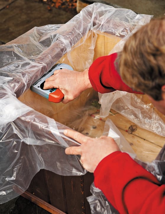Roger Cook staples a plastic sheet lining to waterproof a base container for a live Christmas tree.