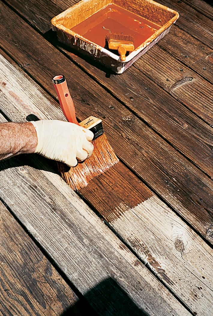 Using a paintbrush to stain a wooden deck.