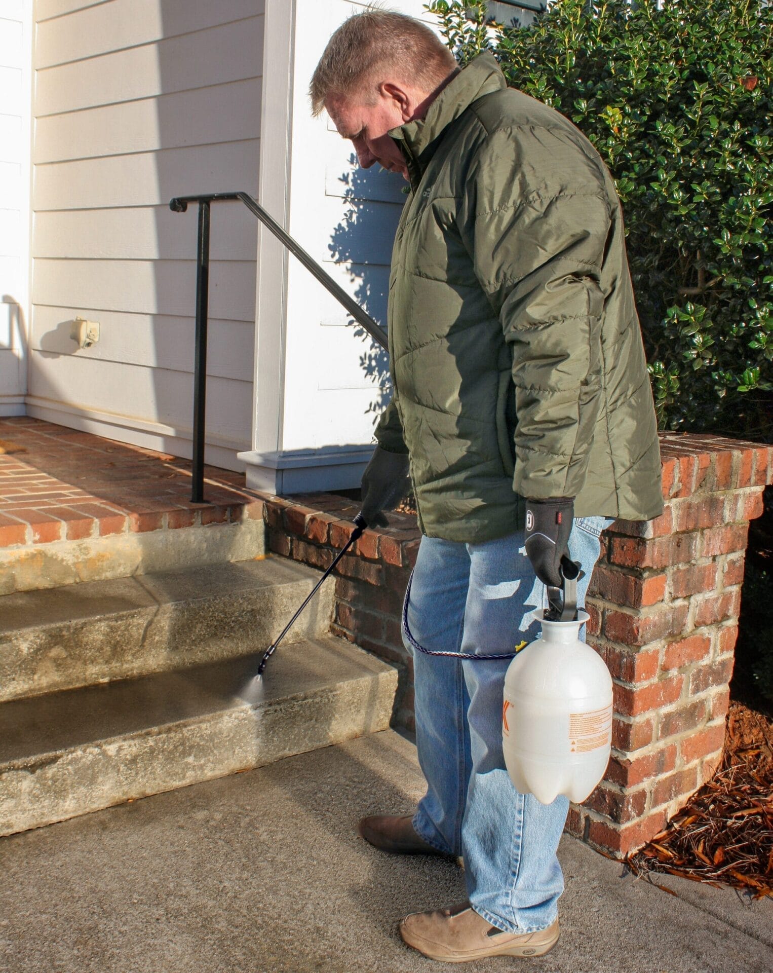 Photo of a man spraying a pet-safe ice prevention method on outdoor stairs
