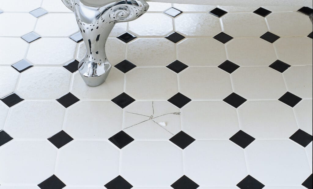 A bathroom floor with a broken tile beside a bathtub.