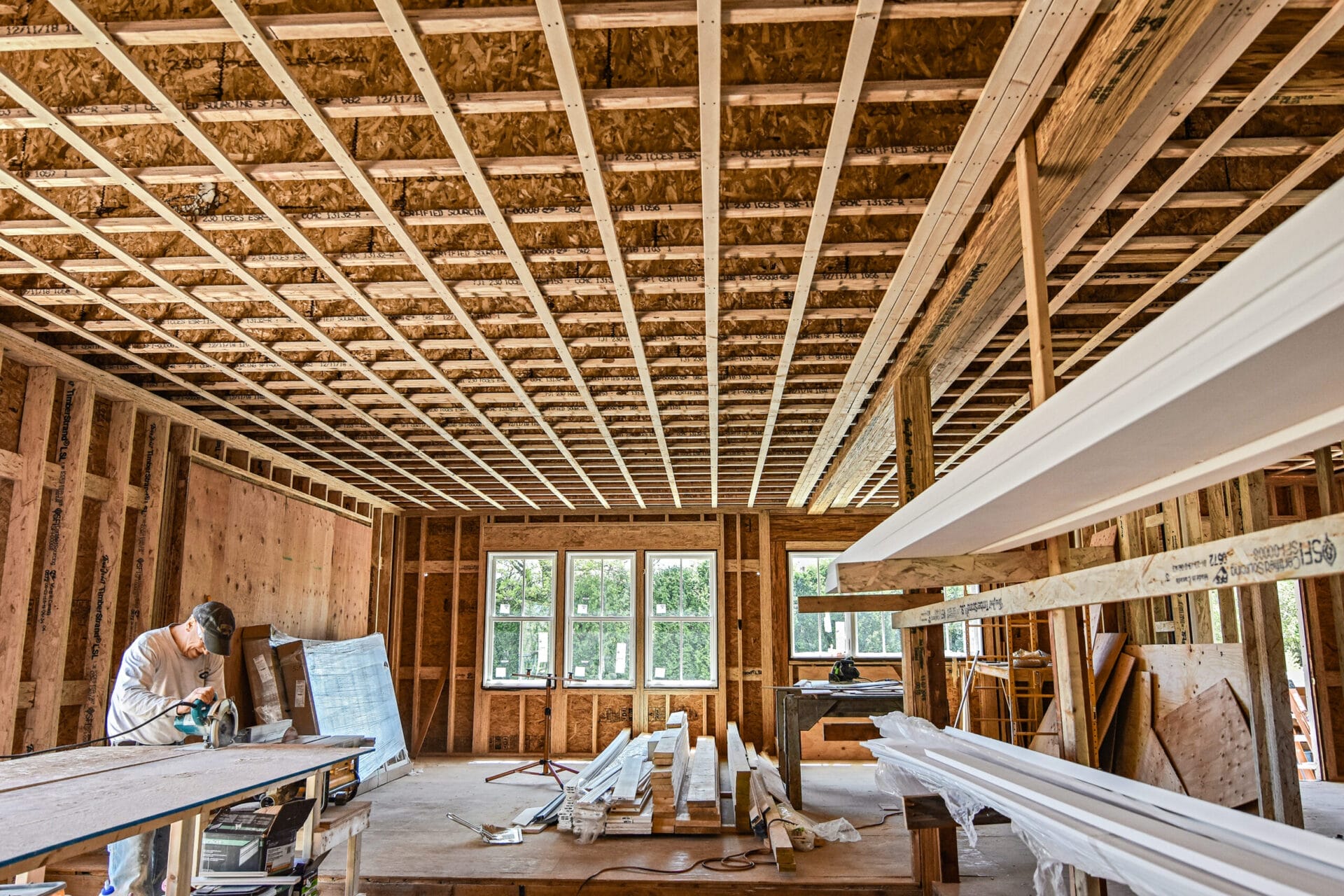 Wayne McDowell cutting plywood in open-plan first floor with kitchen windows and patio door opening visible.