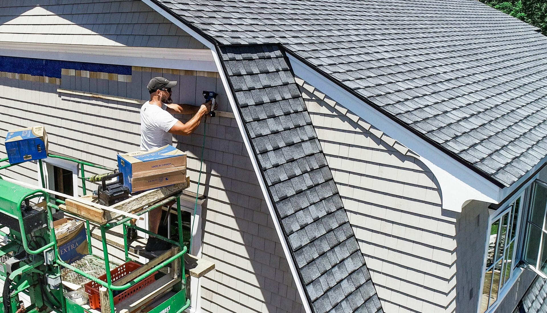 Adam Spink using bucket lift to complete cedar shingle installation on south gambrel gable end.