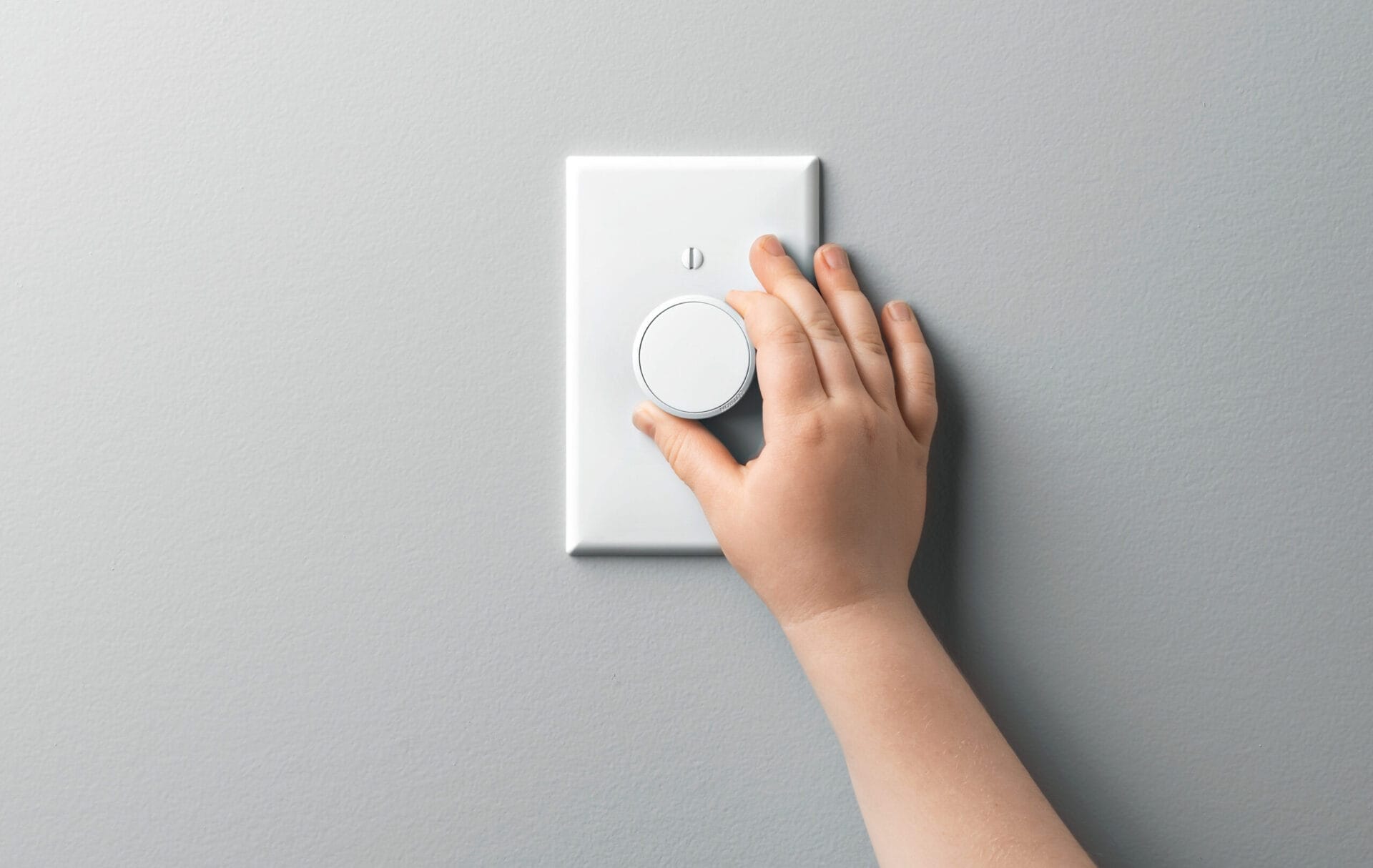 A hand turning the dial on a light dimmer switch.