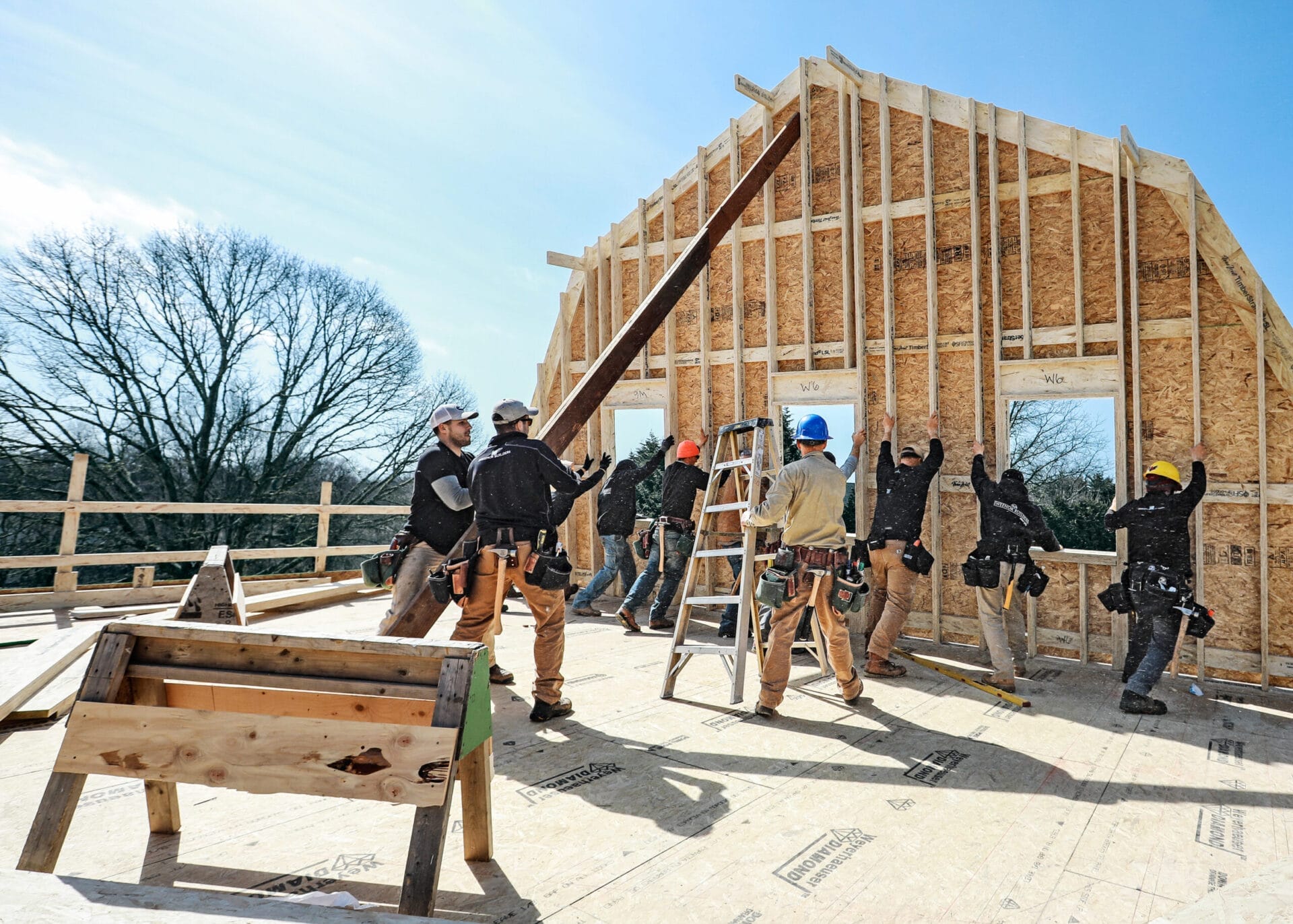 Construction crew raising south-facing gambrel roof end wall built with OSB sheathing and LSL studs.