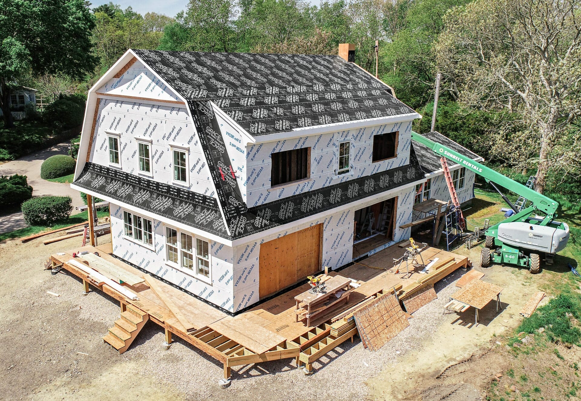Renovated home with gambrel roof and large shed dormers, featuring wraparound deck and shingle siding.