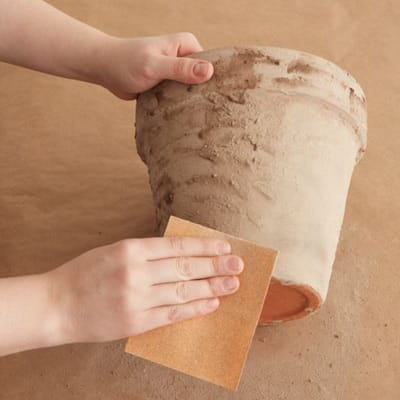 using sandpaper to sand the mixture that was placed on the terra-cotta pot