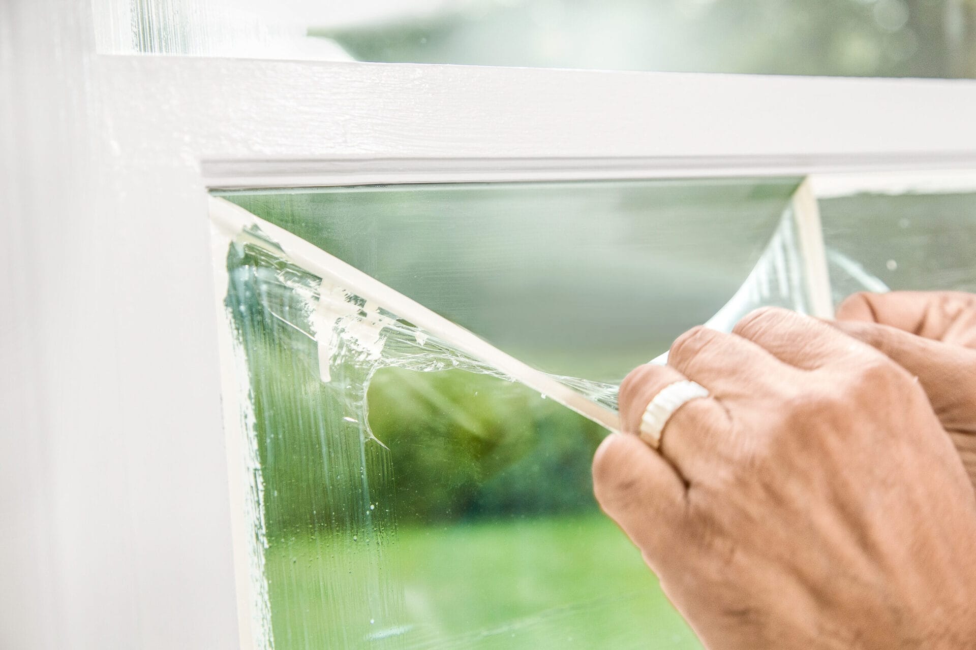 A man removing a masking membrane from a window after painting.