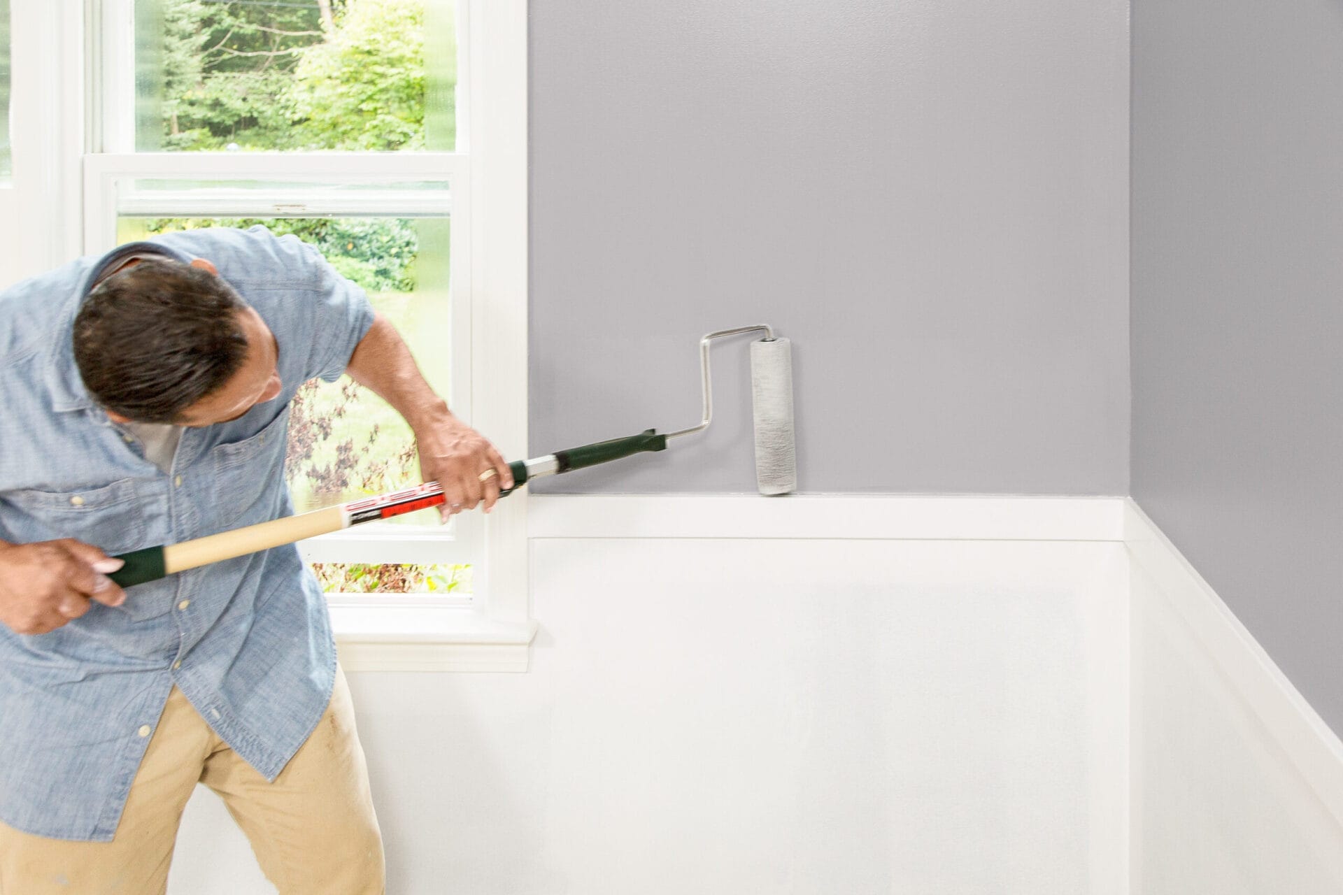 A man using a roller to paint the perimeter of a wall.