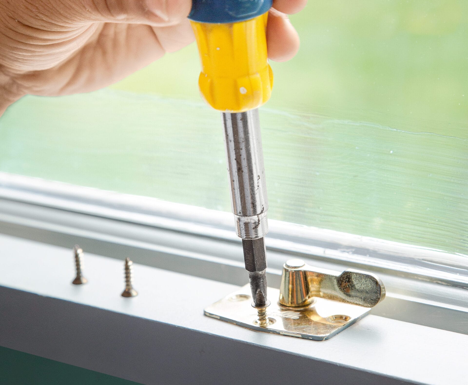 A man using a screwdriver to remove hardware from a window before painting.