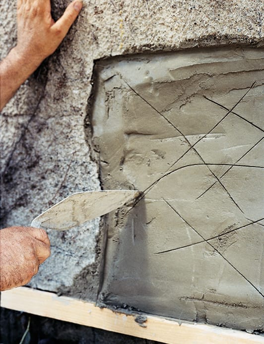 A man scratching the surface of stucco on a wall.