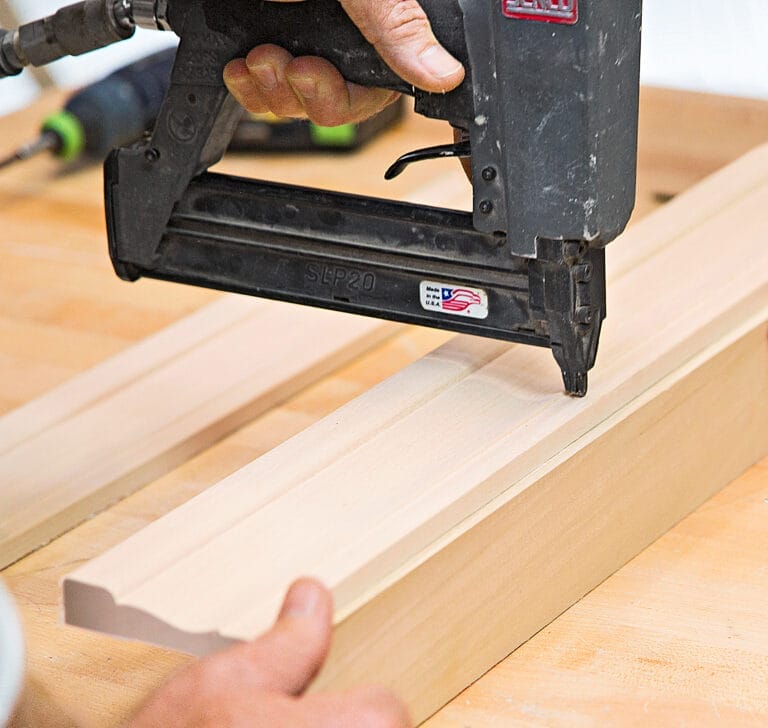 A man uses a nail gun to attach castings to the chalkboard center frame.