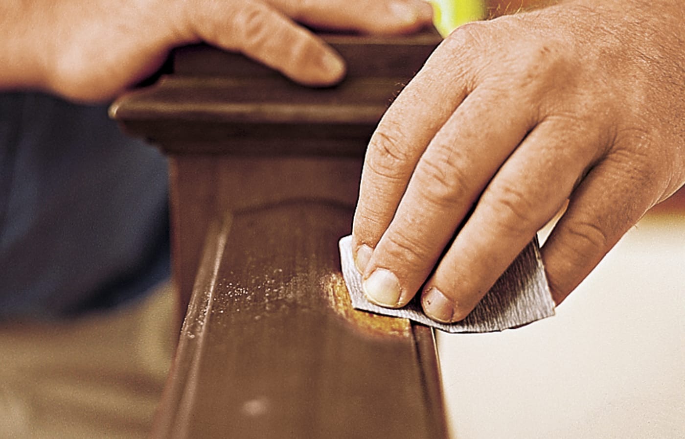 Image of a person sanding the area of a stair railing that needs to be refinished 