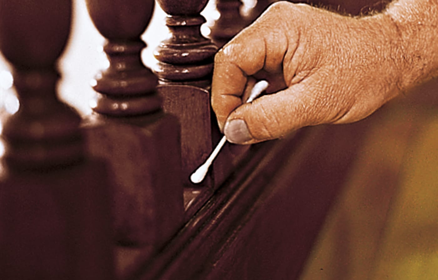 Image of a person testing the existing finish on a stair railing to confirm if it is shellac