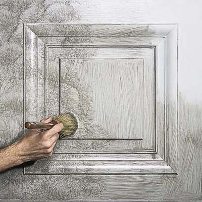 Person applying tinted glaze to painted panel using glazing brush in X pattern.