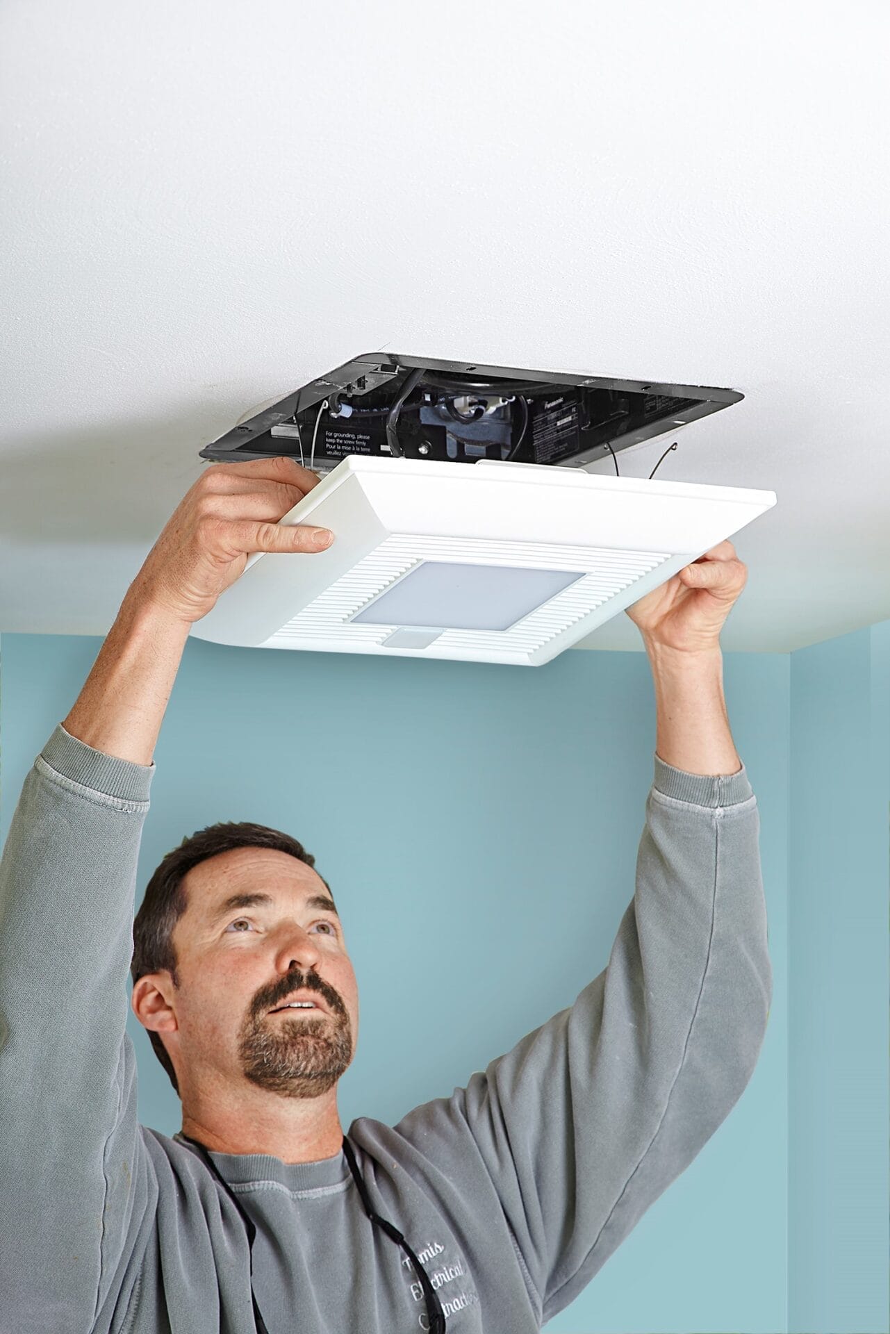 Worker installing bathroom vent fan.