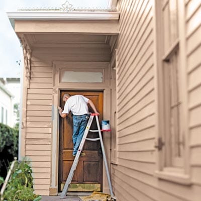 Man on a ladder painting a door.