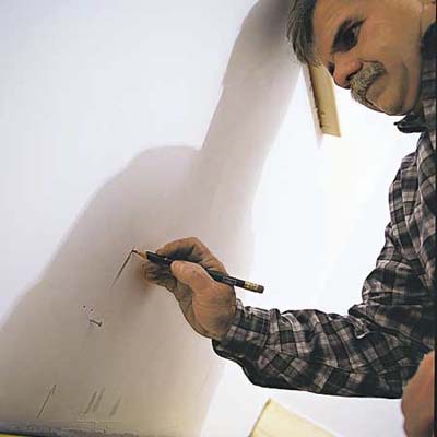 A man marks measurement on the wall to install baseboards.
