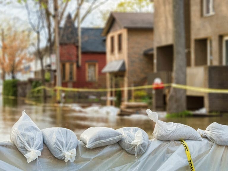 A pile of bags in front of taped off houses after a natural disaster.