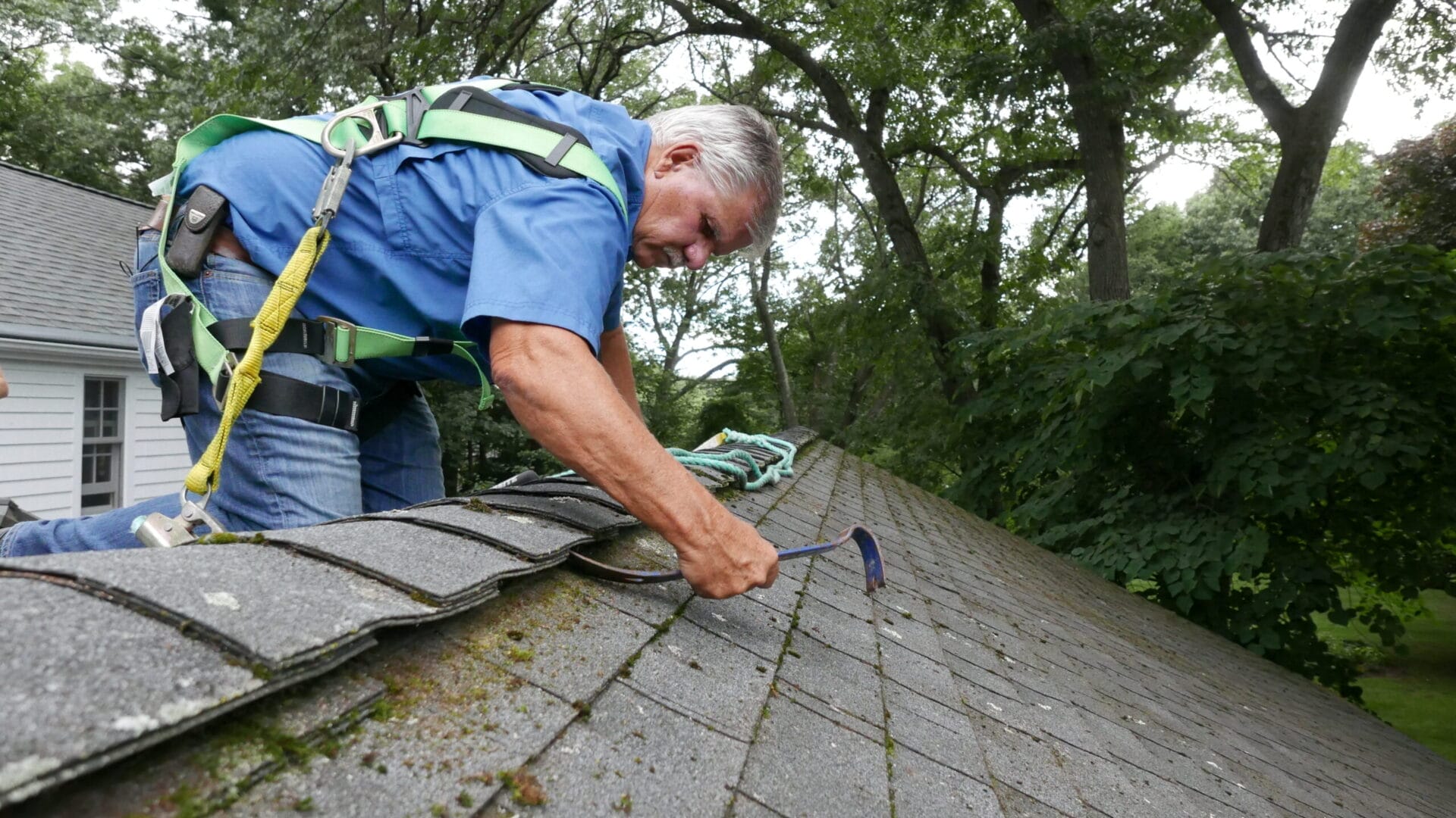 A man working on a roof with a crowbar, he is wearing a safety harness.