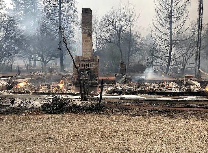 Smoldering remains and debris scattered across burned residential lot.