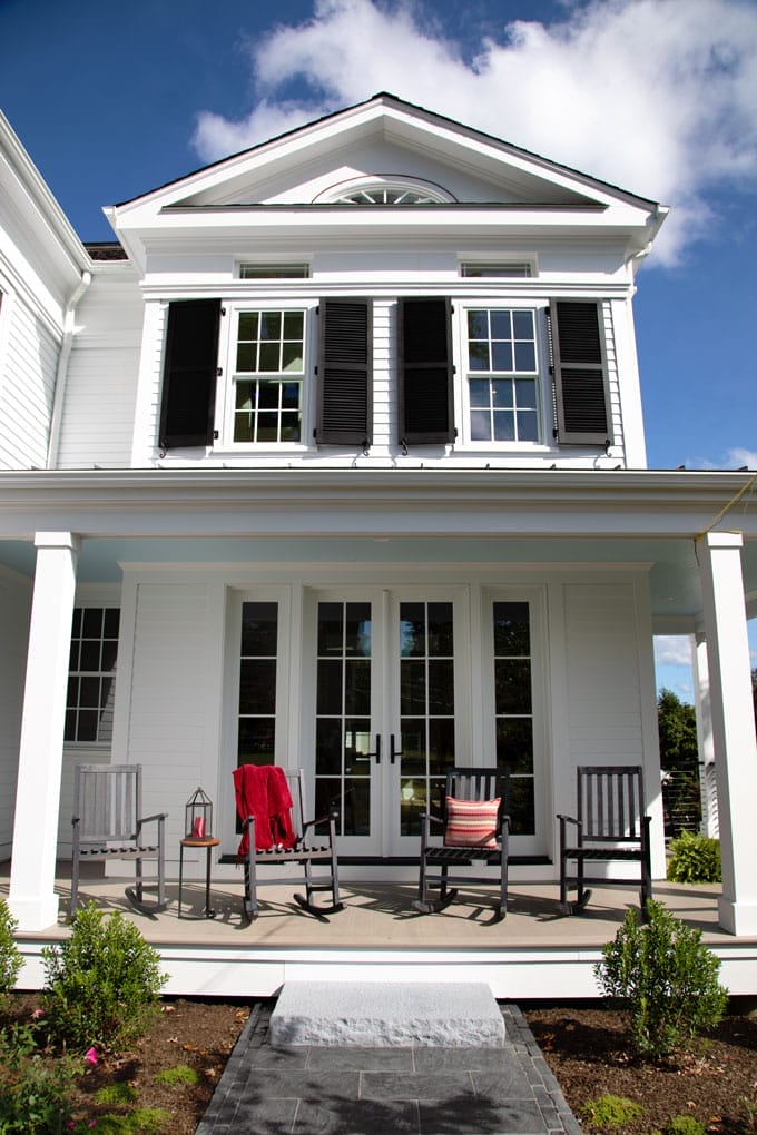 Front porch on a large white house with rocking chairs.