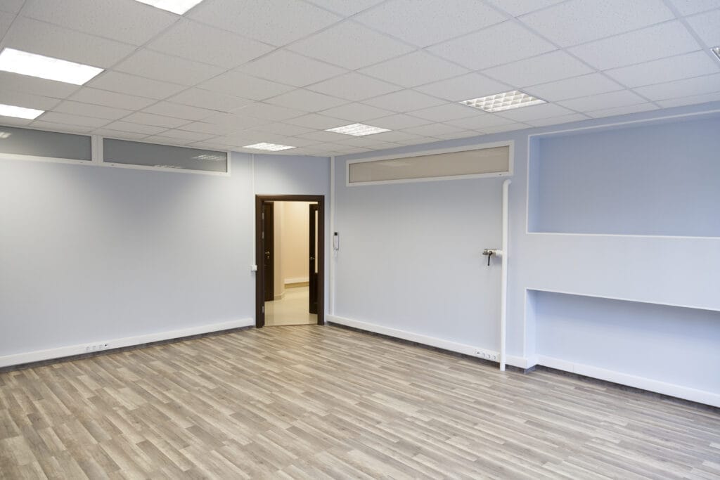 An empty room with an open door in the corner and a drop ceiling.