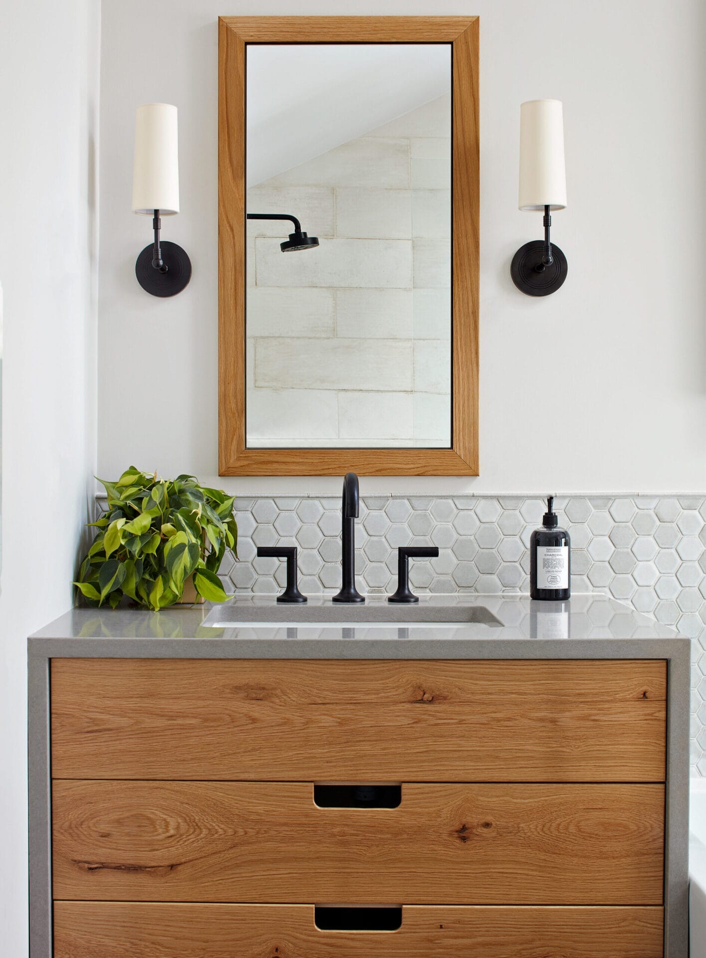 A small bathroom with 2 light fixtures and a mirror hanging over the sink.