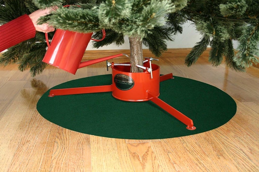 A red Christmas tree stand on a green mat.
