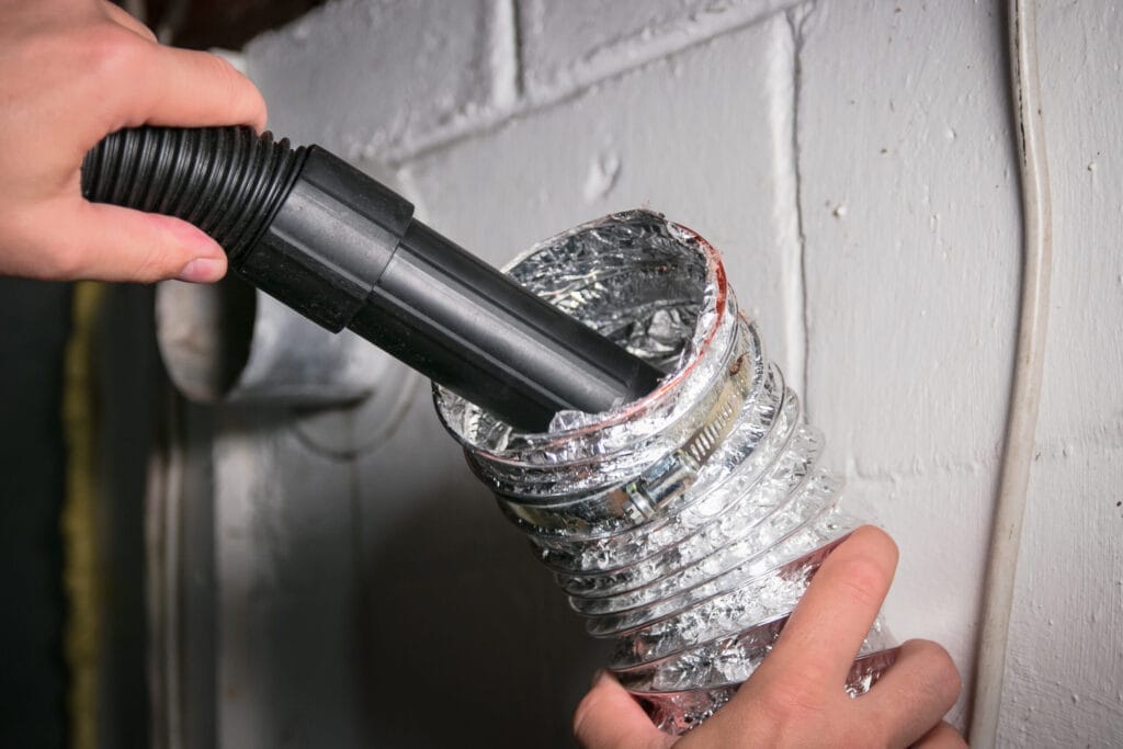 A person cleaning a dryer vent with a vacuum.