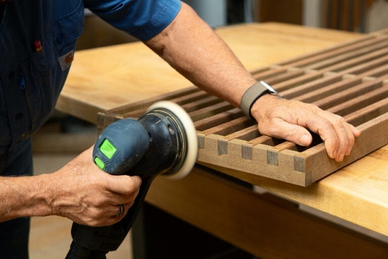 A man trims the slat ends while building a modern platform bench.