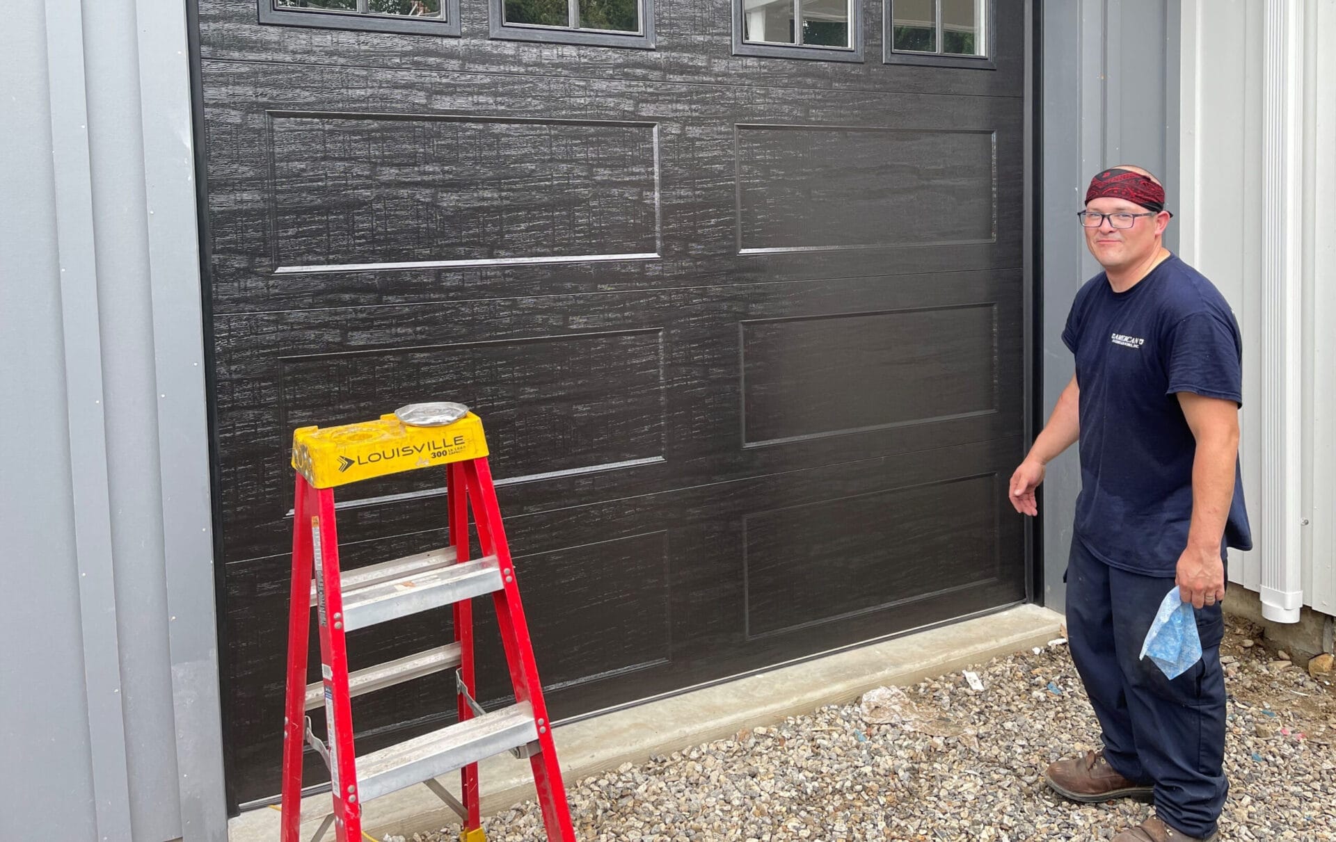 Worker stands in front of clopay steel garage doors with wood-grain pattern.