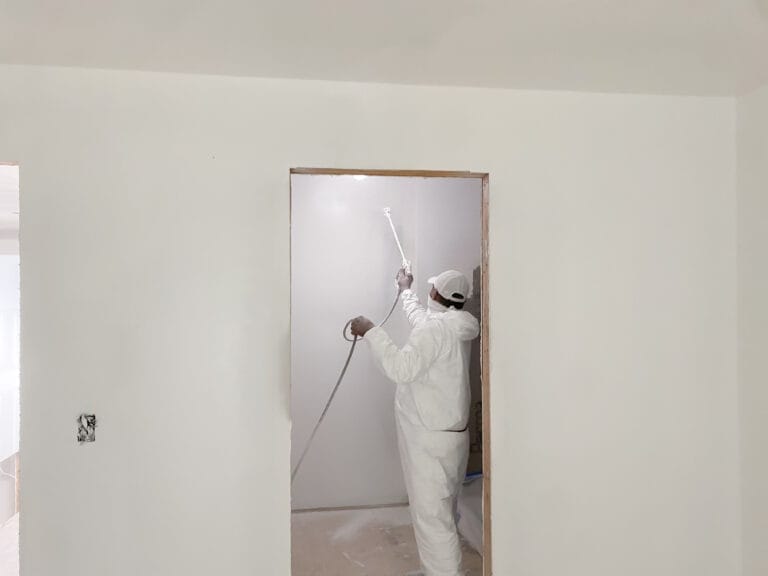 Protected worker spray painting primer on walls and ceilings.