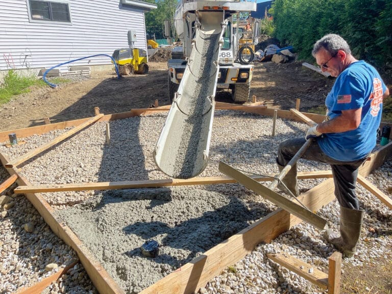 Cement mixer pouring a concrete pad as a man watches.