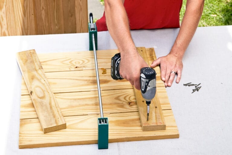 Drilling a piece of wood perpendicular to four pieces of would to make a side of a rain barrel.