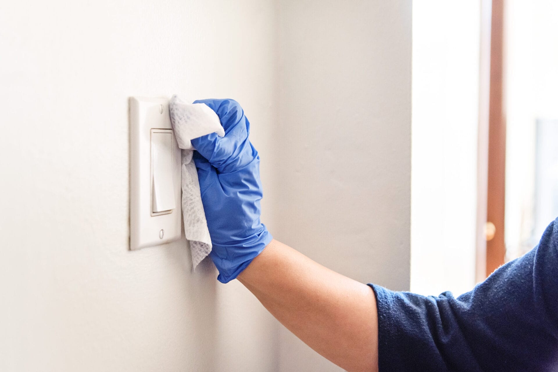Cleaning a light switch with gloves and a damp cloth.