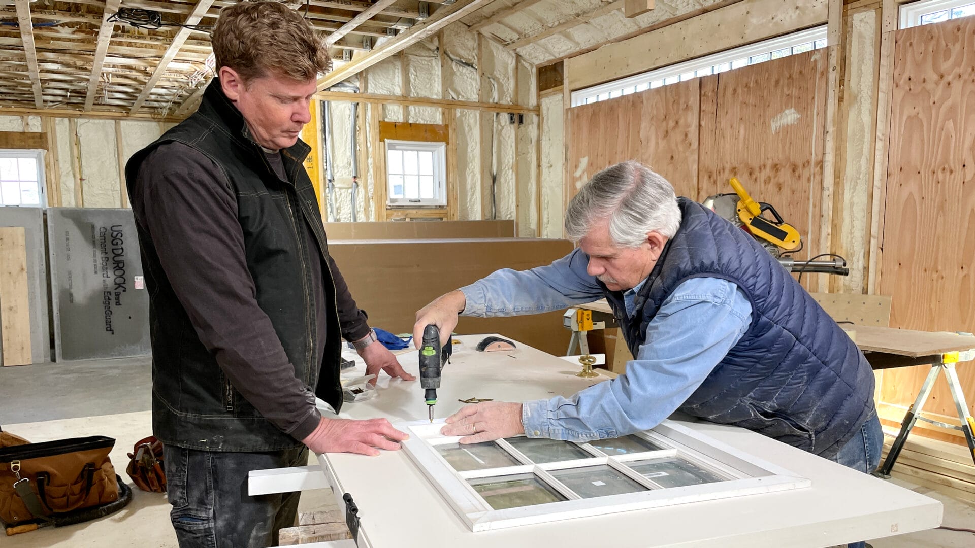 S44 E24, Kevin O'Connor assists Tom Silva with installing a new window sash in the entry door of the garage