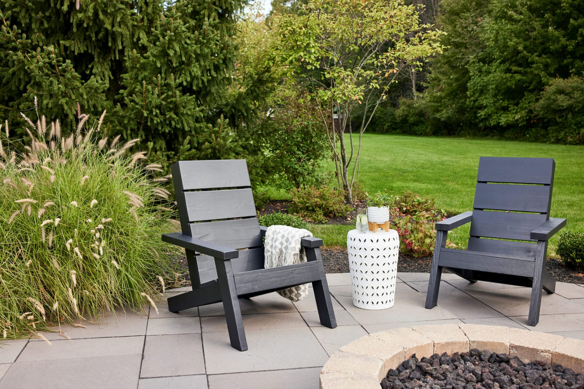 Two modern adirondack chairs painted black in a back yard.